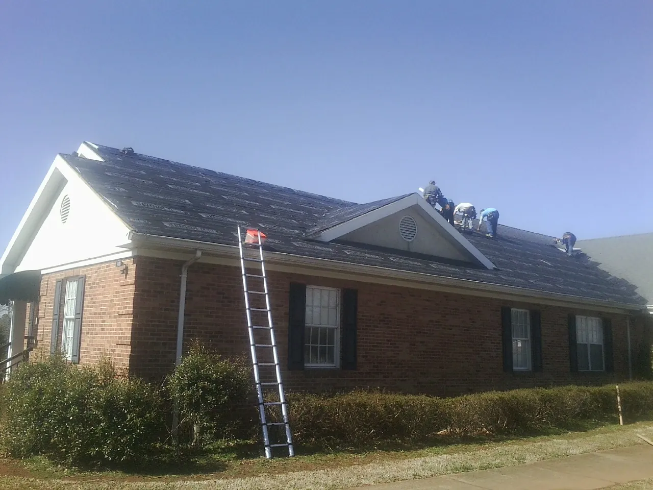 Crew tearing shingles off a brick ranch roof with a ladder set — Emergency Roof Repair work by our crew in Towanda