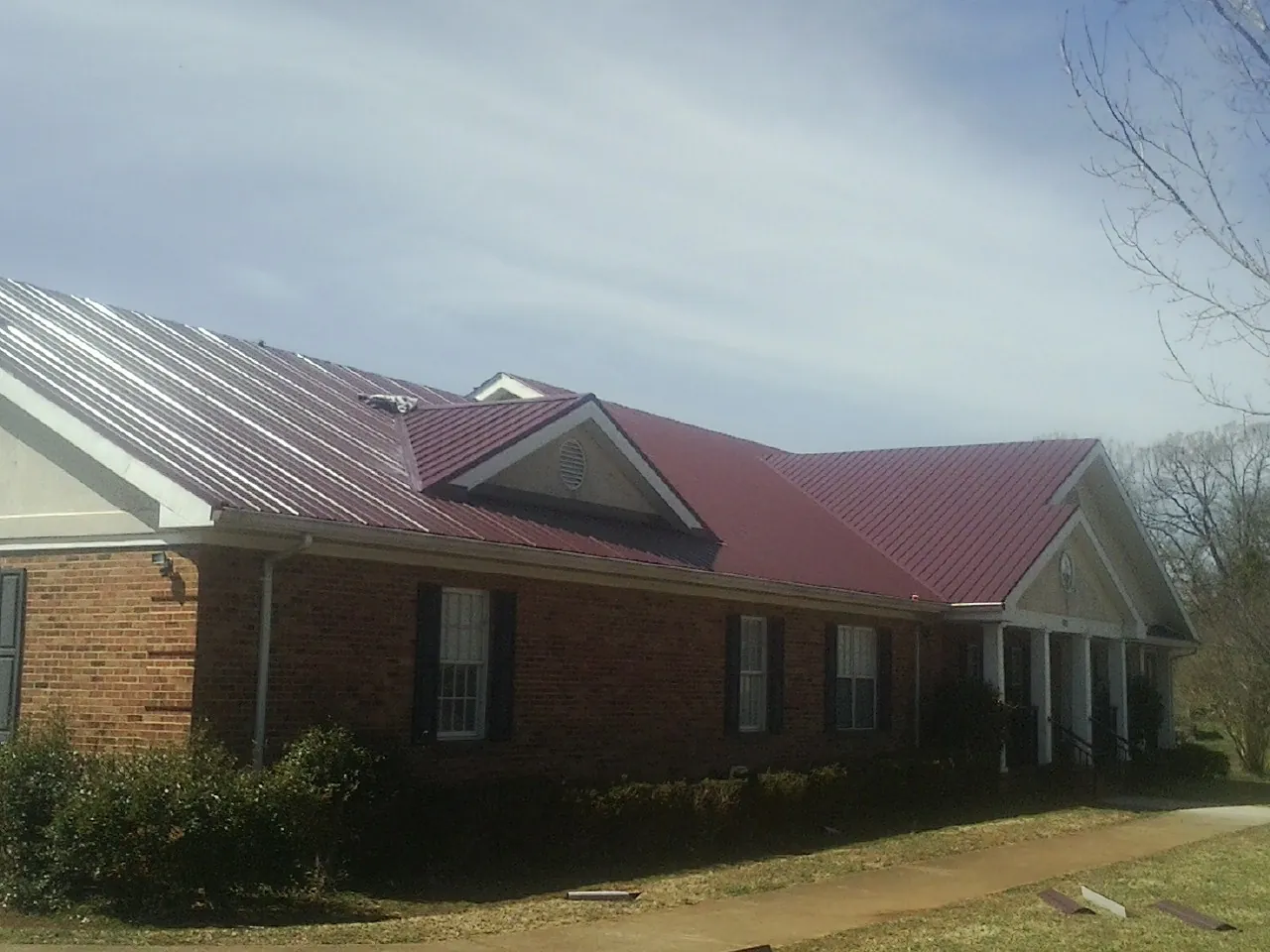 Red metal roof with gabled entries on a long brick building, from a Hail Damage Roof Repair job in Towanda
