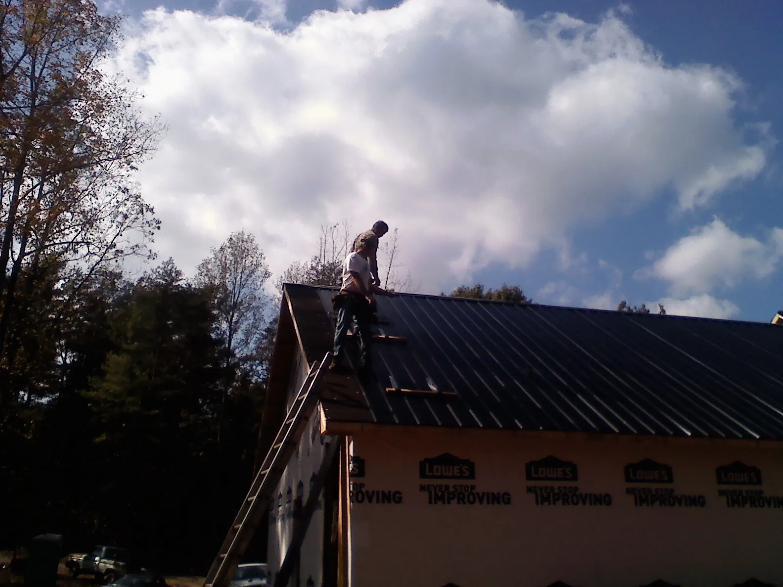 Roofer fastening dark metal panels high against a cloudy sky, from a Roof Inspection job in Towanda