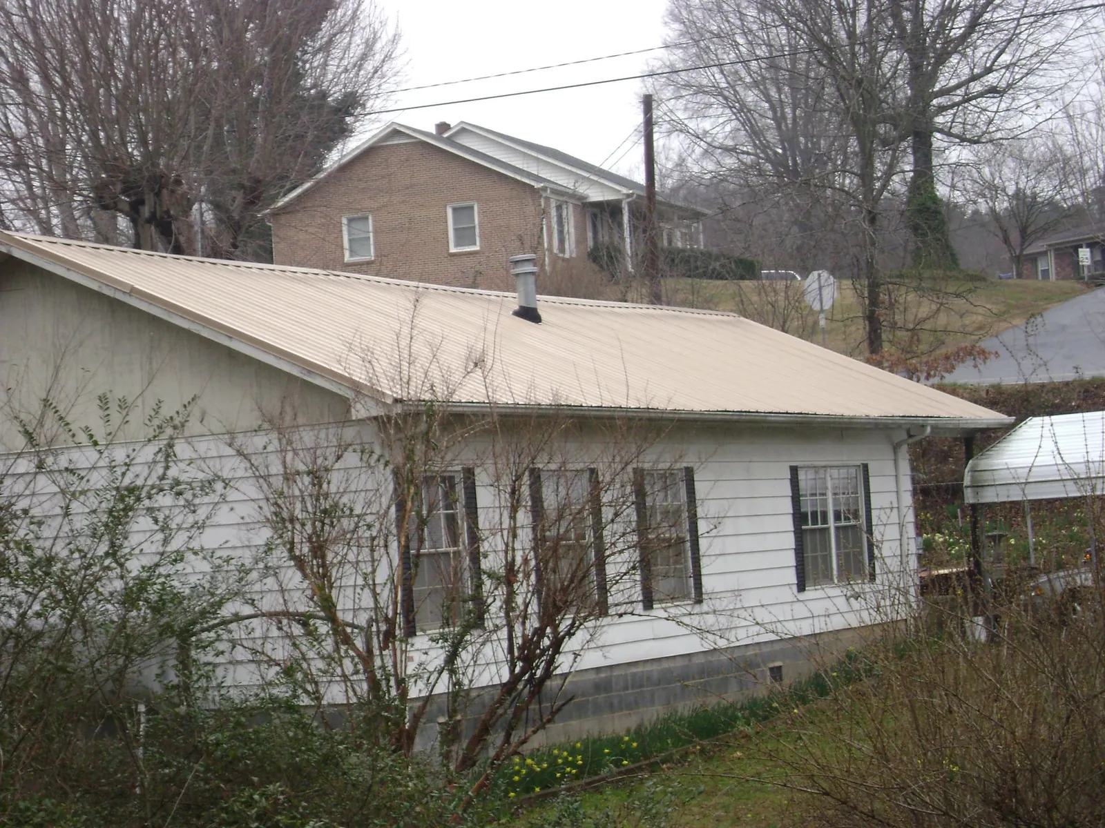 Tan metal roof on a white sided house set into a hillside — Commercial Roofing by Roofing Brothers in Towanda